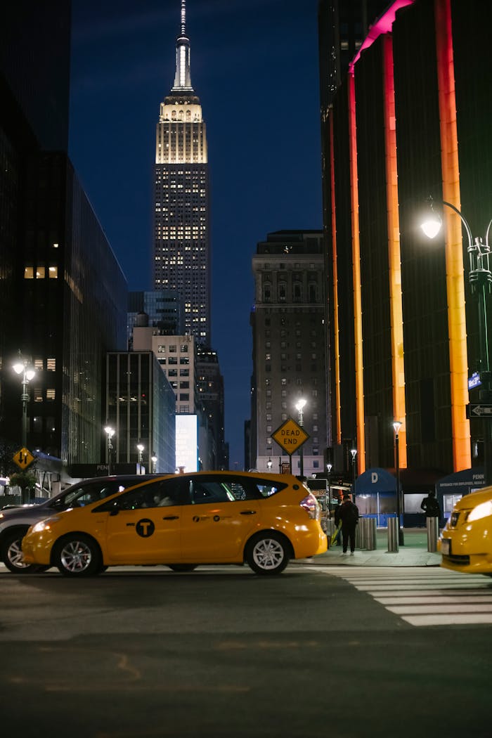 Yellow taxis and the Empire State Building in a bustling New York City street at night.