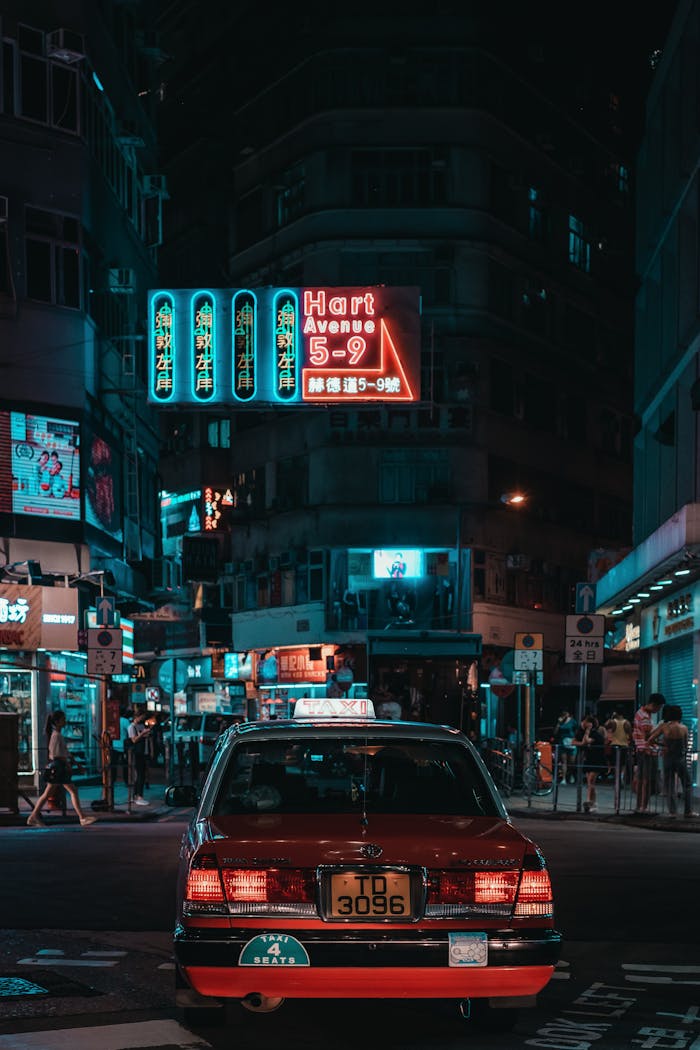 Vibrant nighttime street view in Kowloon, Hong Kong, featuring neon signs and a taxi.